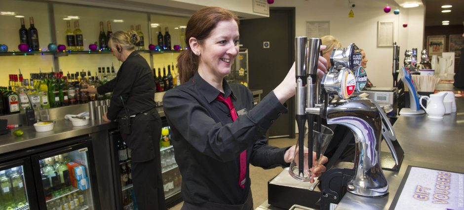 A bartender wearing black shirt and red neck tie is pouring beer on tap